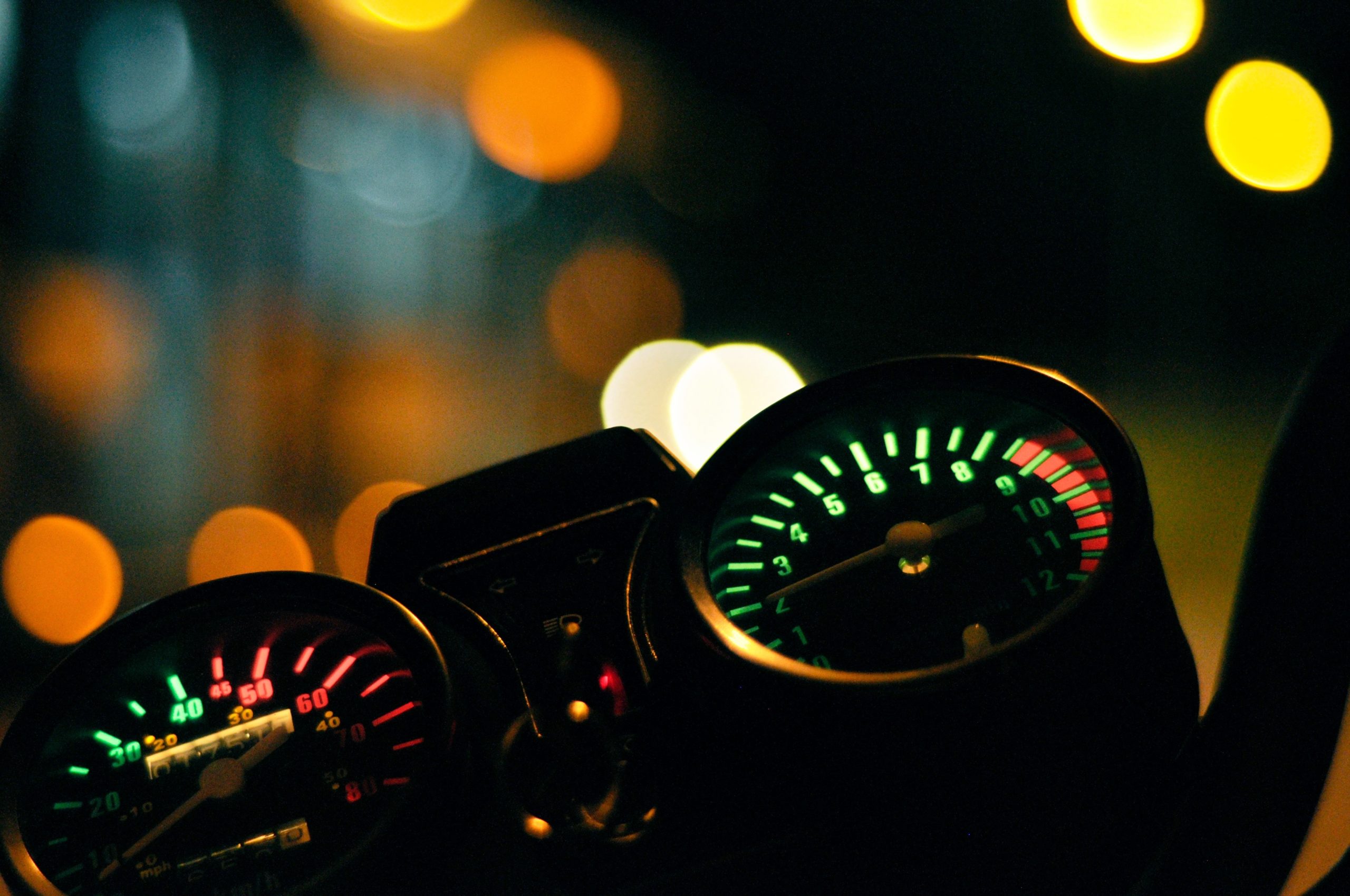Closeup shot of the odometer of a motorcycle with blurred lights in the background at night
