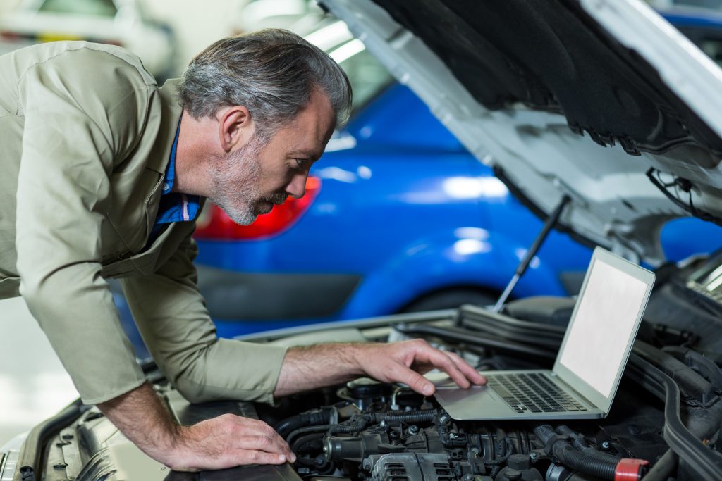 Mechanic using laptop while servicing car engine